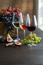 Three Wineglasses Of Red, Rose And White Wine , Grapes In Wicker Basket And Figs On Brown Wood Textured Table 