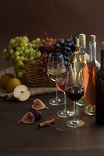 Red, Rose And White Wine Bottles With Three Wineglasses, Grapes In Wicker Basket And Pear Apples And Figs On Brown Wood Textured Table Covered With Canvas Towel