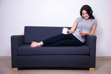 Wall Mural - happy woman sitting on sofa, listening music with mobile phone a