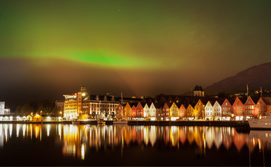 green northern lights above the bryggen hanseatic wharf houses, bergen, norway.