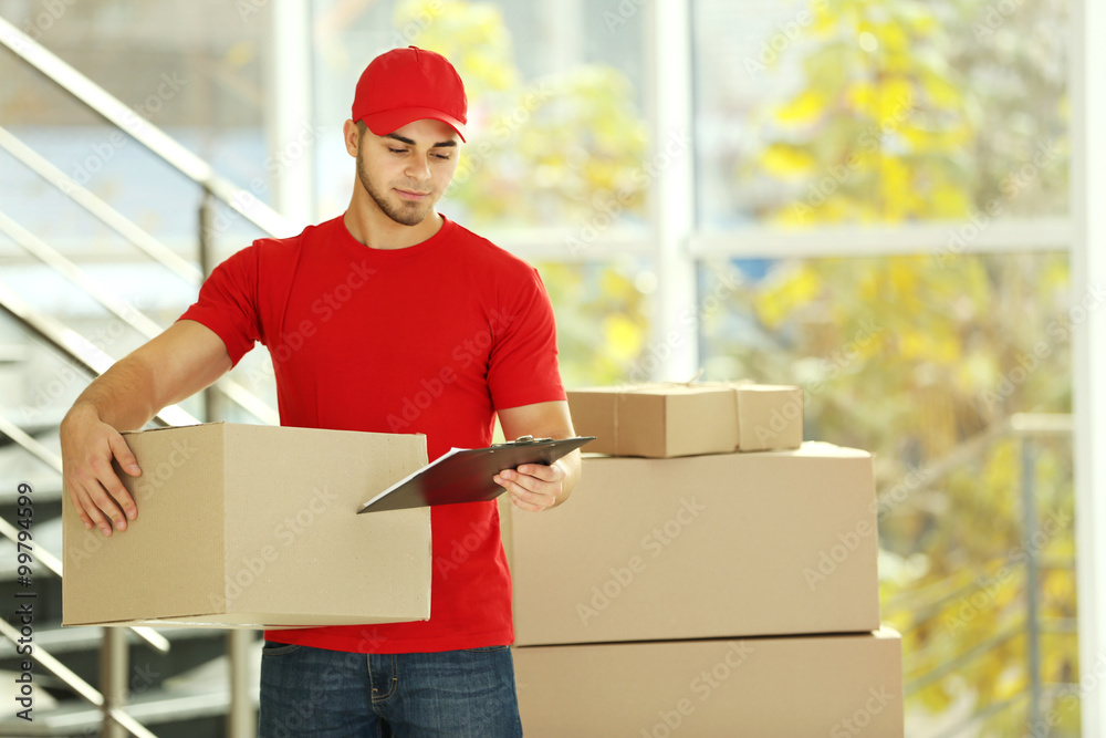 Delivery concept - postman in red uniform holding package near stairs