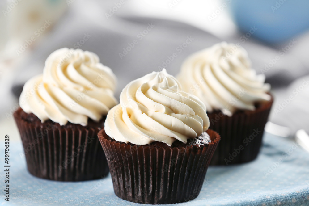 Delicious chocolate cupcakes with cream on served table, close up