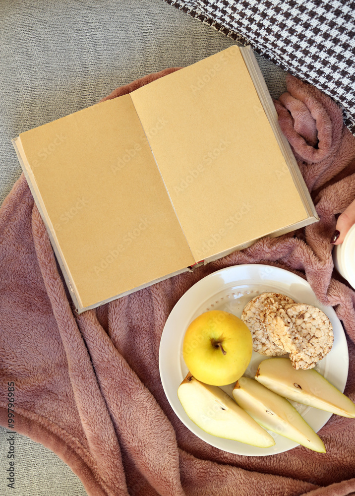 Open book, plaid, fruits and coffee on sofa. Top view