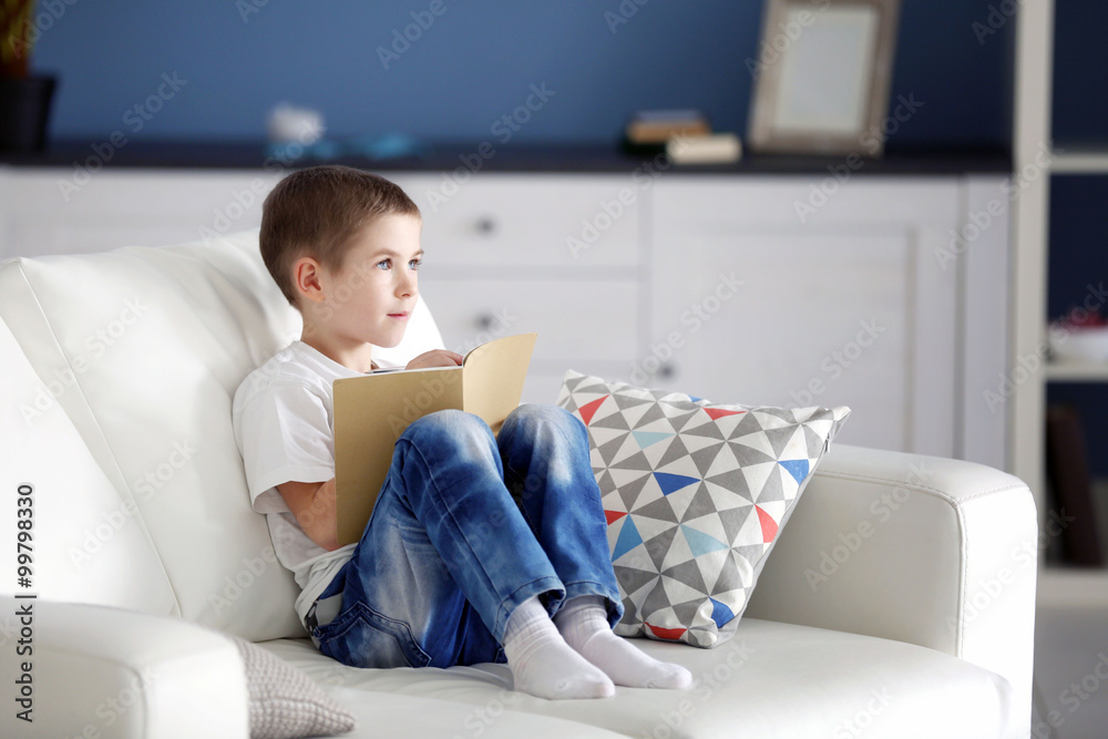 Little boy with notebook and pen sitting on a sofa at home