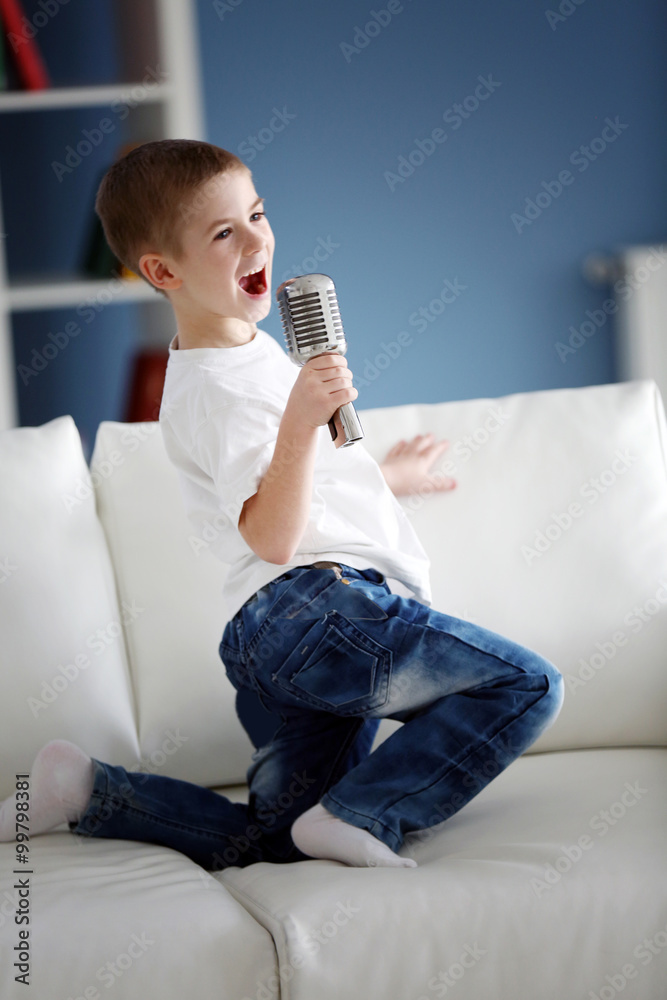 Little boy singing into the microphone on a sofa at home