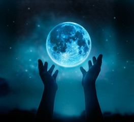 abstract hands while praying at blue full moon with star in dark background