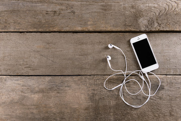 Sticker - White cellphone with headphones on wooden background