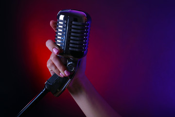 Wall Mural - Female hand holding a retro microphone against colourful background