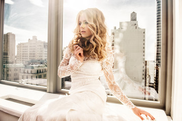 Beautiful fashion model bride sitting near the window with city view wearing white wedding dress