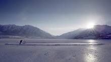 Youth Practicing Ice Hockey Early Morning On A Frozen Mountain Lake.