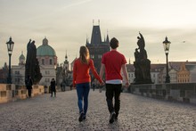 Loving Couple Walking Down The Charles Bridge In Prague At Sunset
