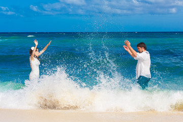 happy bride and groom having fun in the waves on a tropical beac