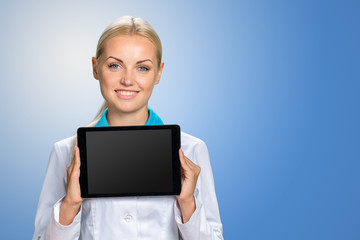 Young cheerful woman doctor is showing her blank tablet