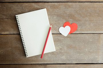 A pencil on a notebook and a red heart  with morning light in vi