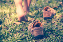Child Take Off Shoes. Child's Foot Learns To Walk On Grass