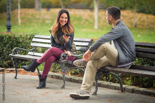 Two Young People Sitting On Benches In A Park And Talking Buy