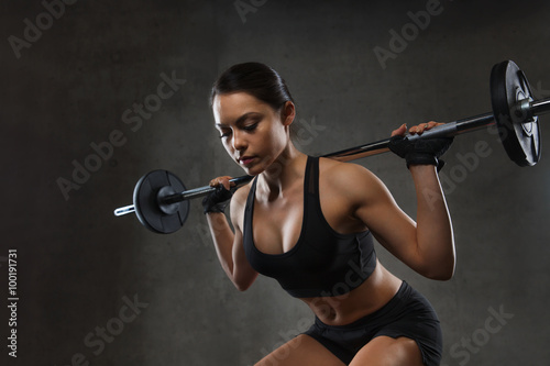 Fototapeta na wymiar young woman flexing muscles with barbell in gym