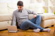 © Mediteraneo - Man listening to music with earphones on laptop computer, sitting on the floor near the sofa