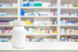 Blank white medicine bottle on counter with blur shelves of drug