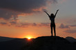 Silhouette of a girl standing on a mountain with his hands up ag
