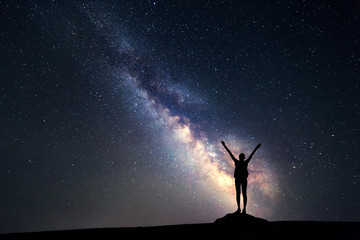 Wall Mural - Milky Way. Night sky with stars and silhouette of a happy woman with backpack and raised up arms. Space background