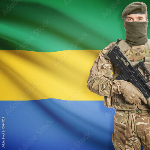 Fotografie, Obraz Soldier with machine gun and flag on background - Gabon