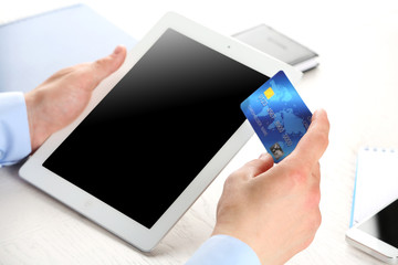 Wall Mural - Man holding credit card and tablet on workplace background