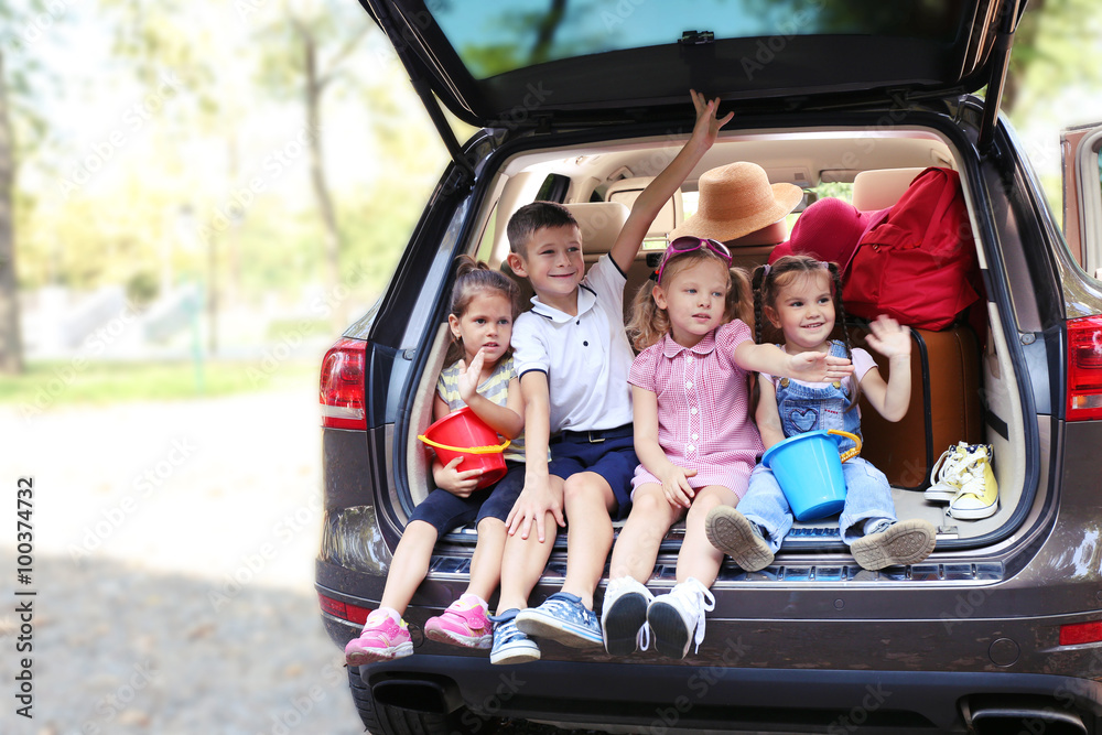 Happy children sit on a car trunk and laughing