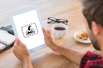 Poster - Composite image of rear view of man using tablet on wooden table