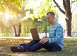 © lkoimages - Young man with laptop sitting in green park