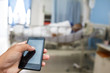 © weerachaiphoto - Hand hold and touch screen smart phone, tablet,cellphone on blur image of A patient in the hospital with saline intravenous, in Asian elderly man hand.