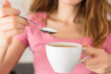 Fototapeta  - Woman adding a spoonful sugar to her coffee