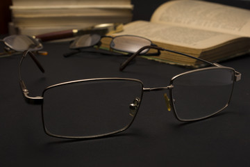 Eyeglasses with magnifying glass on dark surface with books. High resolution image design for Ophthalmologist concept.