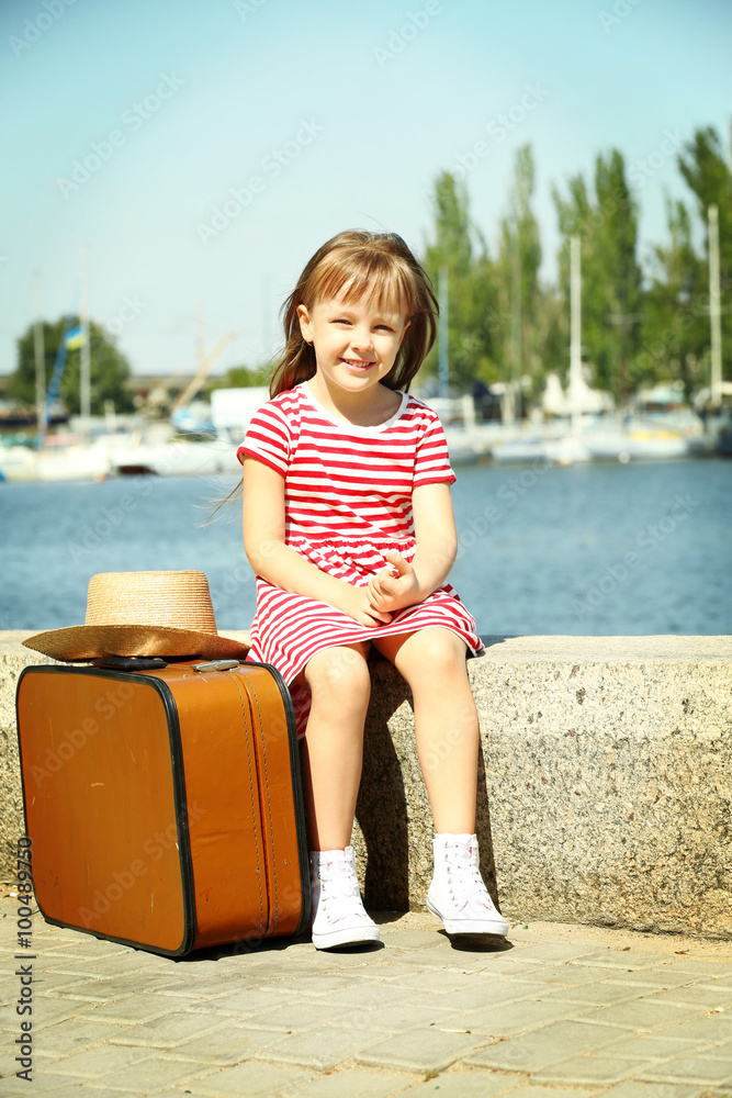 Little girl with suitcase on the riverside