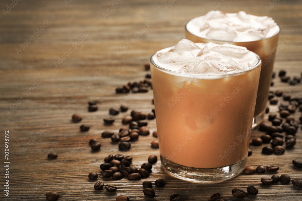 Two cups of ice coffee with coffee beans on wooden table