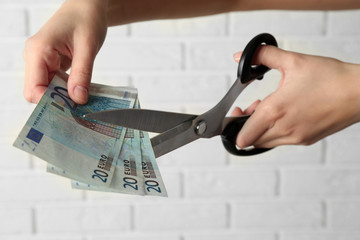 Wall Mural - Hands with scissors cutting money on white brick wall background