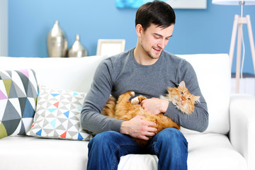 Wall Mural - Young man with fluffy cat sitting on a sofa