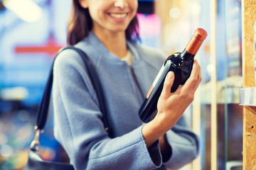 happy woman choosing and buying wine in market