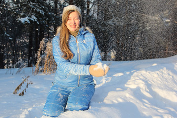 Wall Mural - The woman with long hair in a blue jacket swept up by snow with a snowball in hands against the wood in the winter