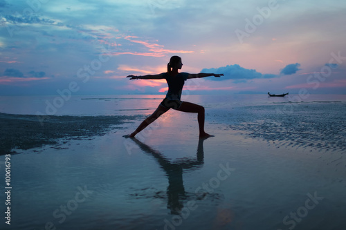 Plakat Sylwetka młodej kobiety ćwiczy joga na plaży przy wschodem słońca