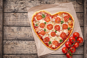 Heart shaped pizza margherita with tomatoes and mozzarella vegetarian meal on vintage wooden table background. Food concept of romantic love for Valentines Day.