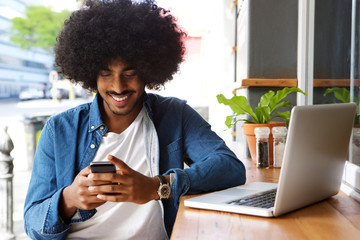 Smiling guy using mobile phone and laptop