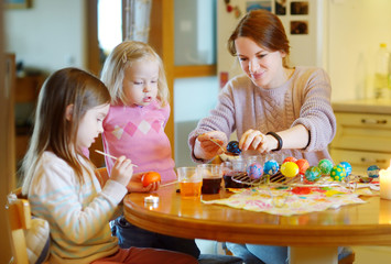 Wall Mural - Young mother and her two daughters painting Easter eggs