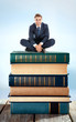 © Africa Studio - Handsome young man sitting on stack of books on table on bright background