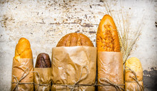 Fresh Bread Wrapped In Paper. On Rustic Background.