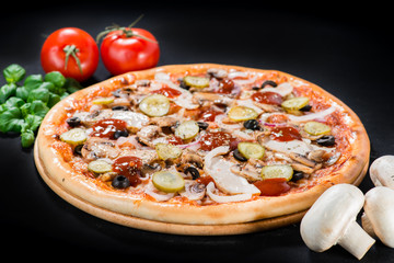 Wall Mural - closeup Tasty pizza with tomatoes, mushroom, sausage, basil and chili pepper on a black background (shallow DOF)