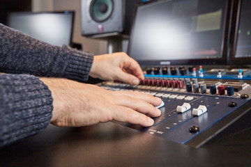 Side view of hands of audio engineer mixing on console