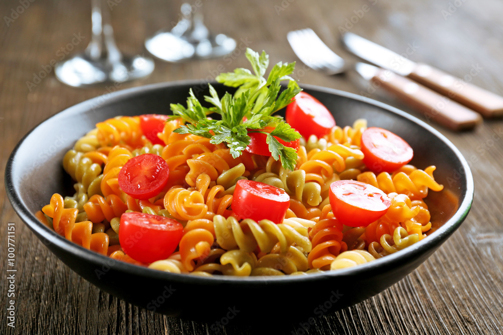 Delicious macaroni dish in black bowl on served wooden table