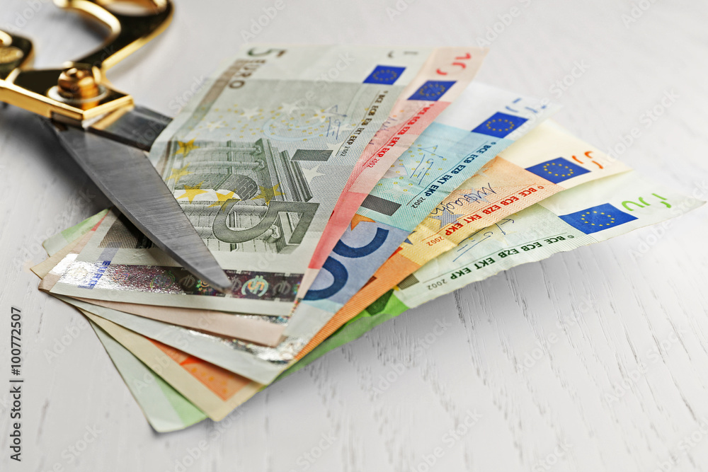Scissors cuts different euro banknote on table