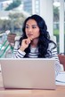 Attractive Asian woman using laptop with hand on chin